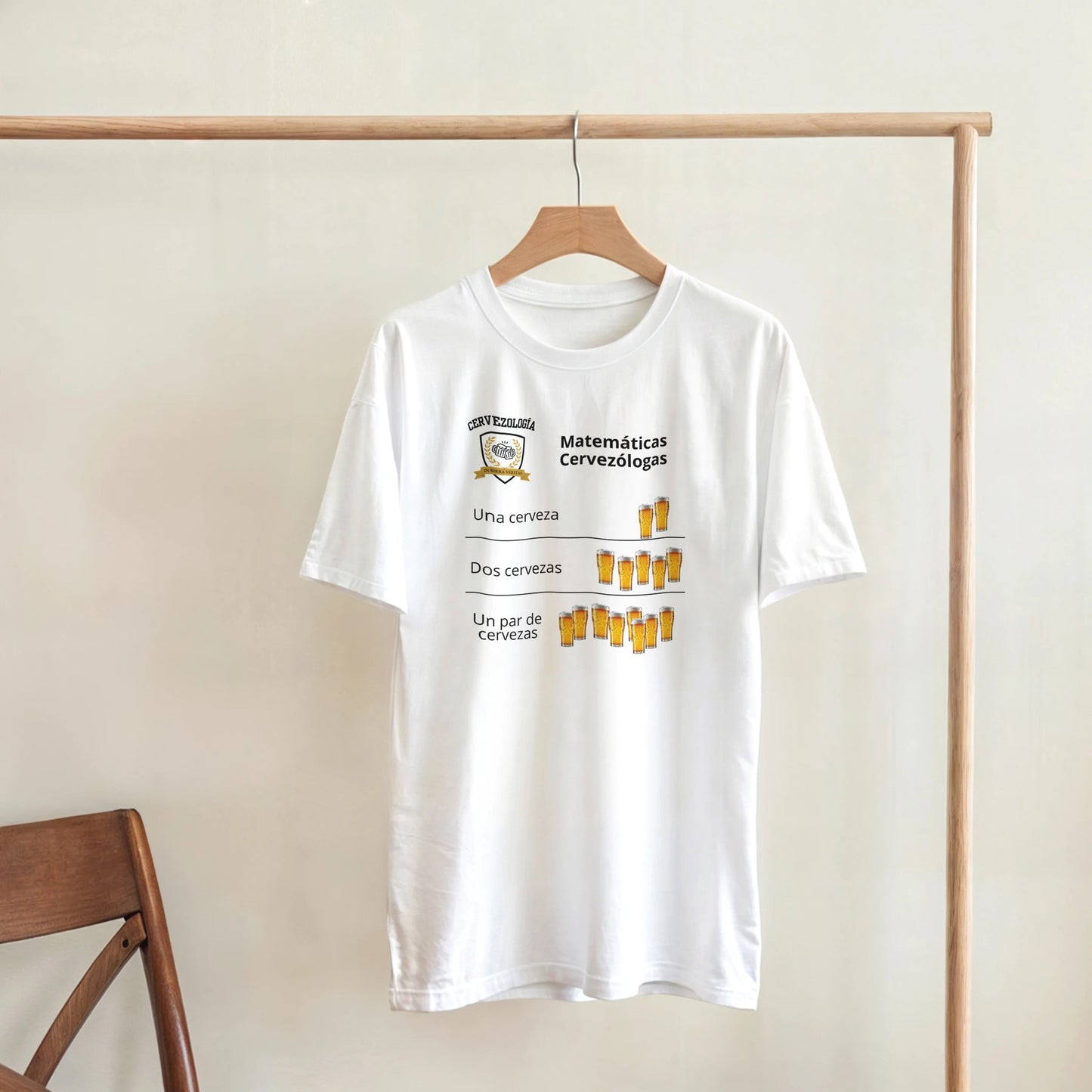 Camiseta blanca colgada en percha con diseño de cervezas y texto “Matemáticas Cervezólogas”.