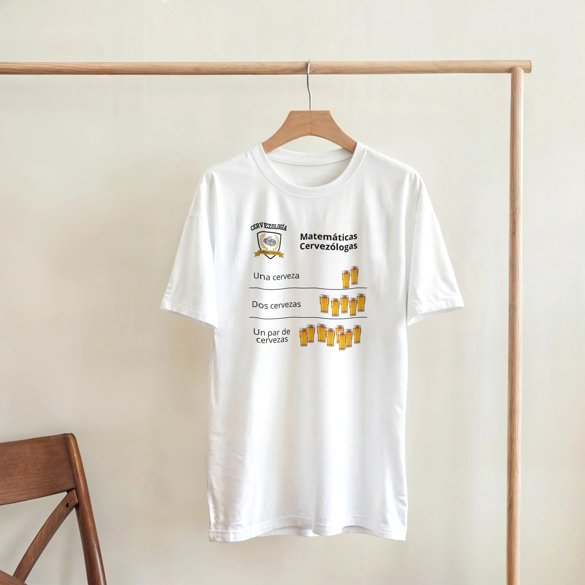 Camiseta blanca colgada en percha con diseño de cervezas y texto “Matemáticas Cervezólogas”.