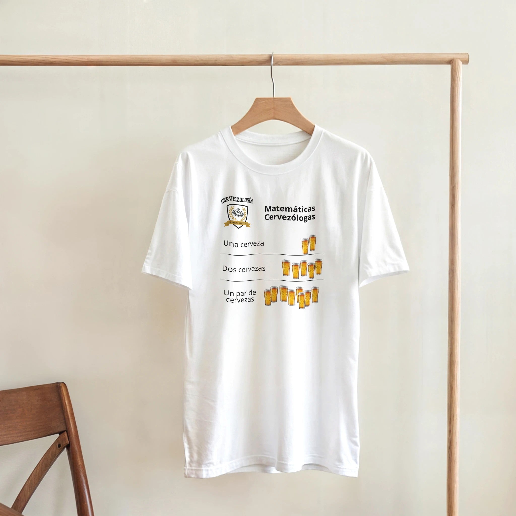 Camiseta blanca colgada en percha con diseño de cervezas y texto “Matemáticas Cervezólogas”.