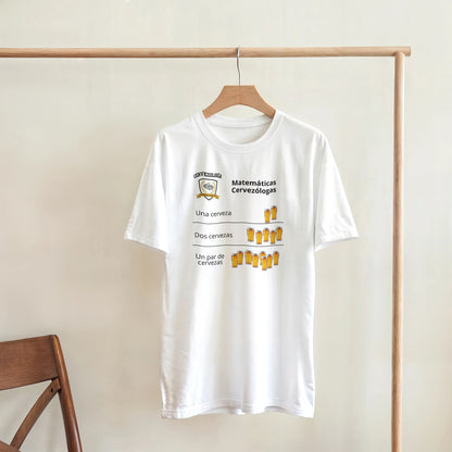 Camiseta blanca colgada en percha con diseño de cervezas y texto “Matemáticas Cervezólogas”.