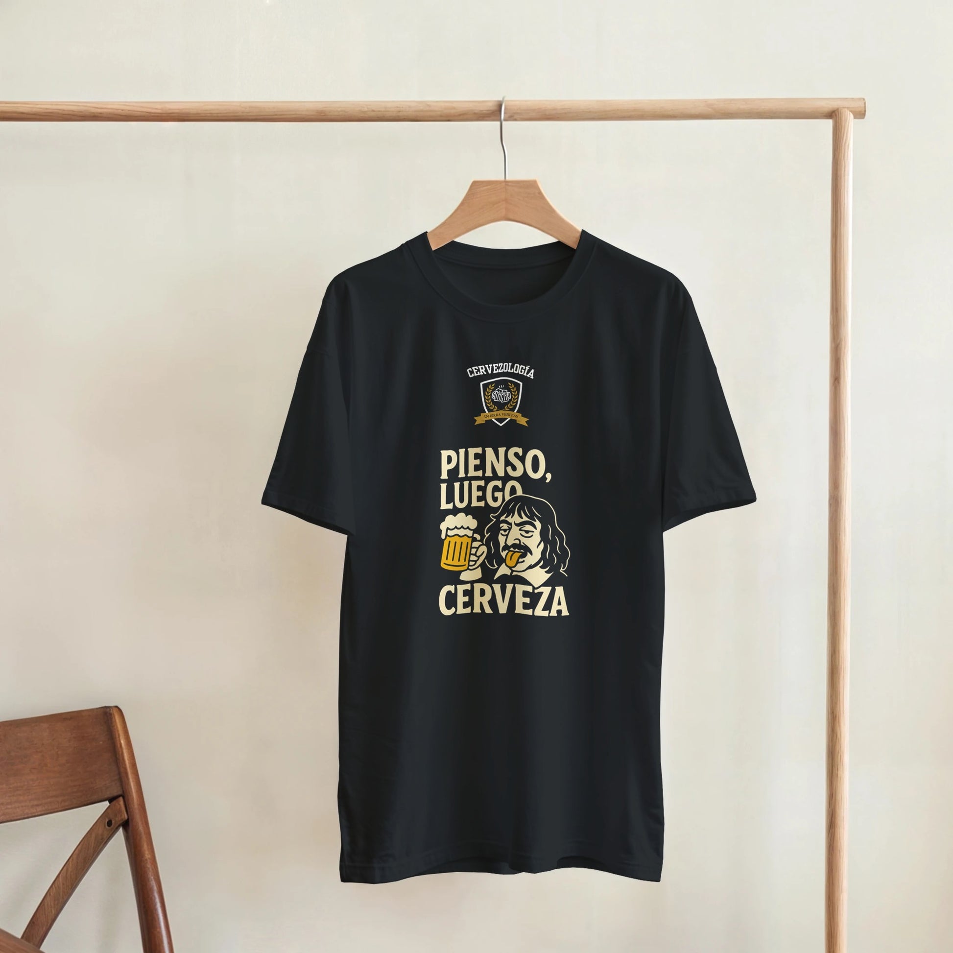 Camiseta negra colgada en percha con estampado “PIENSO, LUEGO CERVEZA” dorado